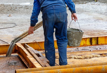 A man in a blue jumpsuit is holding a bucket and a broom. He is cleaning a dirty areaの写真素材