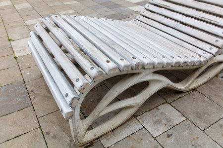 A white bench with a wooden frame is on a brick sidewalk. The bench is long and narrow, and it is leaning against the wall. The bench is empty, and it looks like it has been there for a whileの写真素材