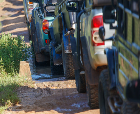A group of vehicles are parked on a dirt road. The vehicles are all different sizes and colors, including a green truck and a white truck. The scene is muddy and wetの写真素材