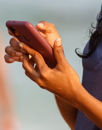 A woman is holding a cell phone in her hand. She is looking at the screen and she is texting or...