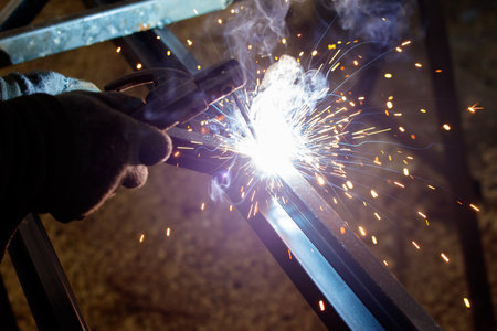 A man is welding metal with a torch. The sparks and smoke from the welding process create a sense of...