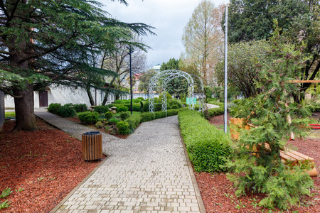 A brick walkway with a bench and a gazebo in the middle. The walkway is lined with trees and bushesの写真素材