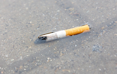 A cigarette butt is floating in a puddle of water. The cigarette is half burned and has a white label on it. The scene is somewhat eerie and unsettlingの写真素材