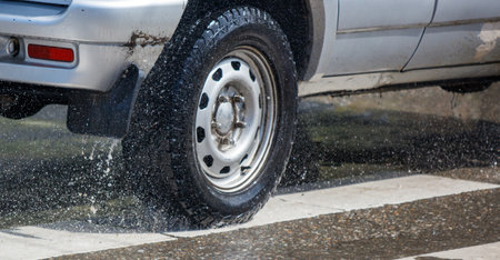 A truck is driving down a wet road with water spraying out from the back. The water is coming out of...