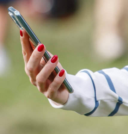 A woman is holding a cell phone with her right hand and her left hand is holding a bottle of nail polishの写真素材