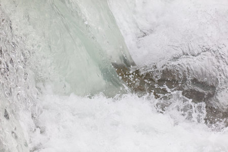 A large body of water with a strong current. The water is white and frozen, with ice and snow floating on top. The scene is dynamic and powerful, with the water rushingの写真素材