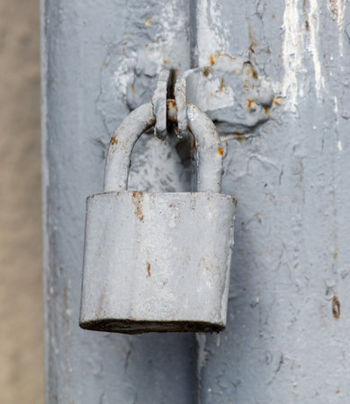 A rusty lock is hanging from a metal pole. The lock is old and worn, and it is hanging from a rusty metal poleの写真素材
