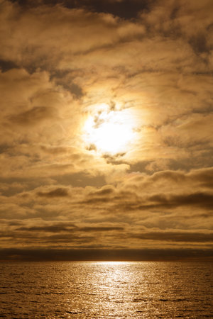 The sun is shining on the water, creating a beautiful and serene scene. The clouds in the sky add a sense of depth and atmosphere to the imageの写真素材