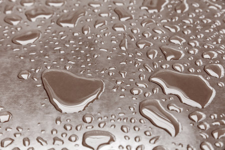 A wet surface with many small drops of water scattered across it. Scene is calm and peaceful, as the drops of water seem to be falling gently and even across the surfaceの写真素材