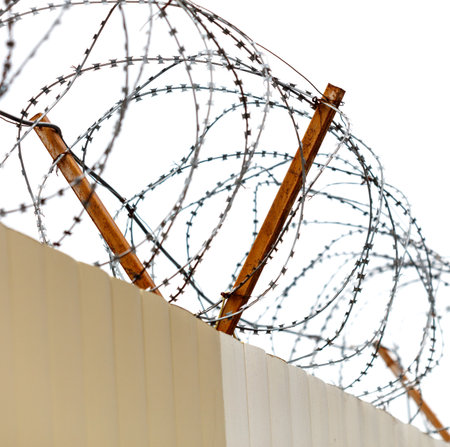 A fence with barbed wire on top of it. The fence is on a buildingの写真素材