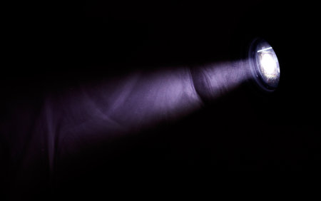A hand is illuminated by a light, casting a shadow on the wall. The image has a moody and mysterious feel to it, as the light seems to be coming from a distant sourceの写真素材