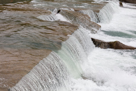 A waterfall with a greenish tint. The water is white and the rocks are brown. The water is flowing down the rocks and creating a misty atmosphereの写真素材