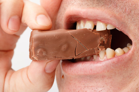A man is eating a chocolate bar with his teeth showing. The chocolate bar is broken in halfの写真素材