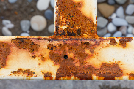 A rusted metal beam with a hole in it. The rusted metal beam is on a concrete surface