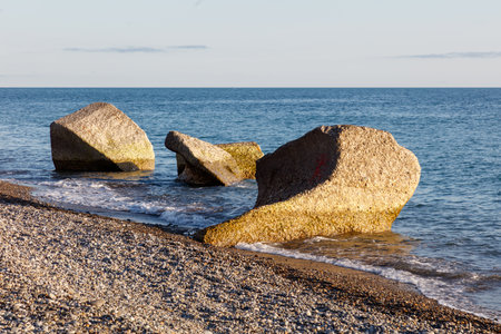 A rocky shoreline with a large rock in the middle. The rock is partially submerged in the waterの写真素材
