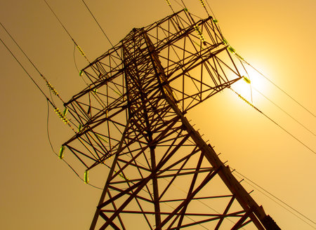 A tall power tower with a sun shining on it. The tower is surrounded by wires and is the tallest structure in the areaの写真素材