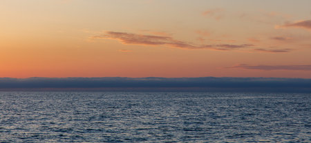 The sky is a beautiful orange color as the sun sets. The ocean is calm and peaceful, with no one in sightの写真素材