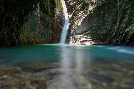 A waterfall is reflected in the water of a pool. The water is clear and calm. Concept of tranquility and serenityの写真素材