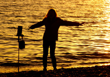 A woman stands on a beach with her arms outstretched, looking out at the water. The scene is serene...