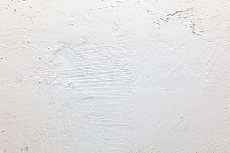 A white wall with a rough texture. The wall is covered in white paint and has a few scratches and marks. Scene is somewhat rough and unfinished, but it also has a sense of potential and possibilityの写真素材