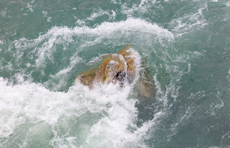 The water is a beautiful shade of blue and the rock is a dark brown color. The rock is floating in...