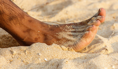 A man's foot is in the sand, with a few grains of sand on it. Concept of relaxation and leisure, as the man is sitting on the beach and enjoying the warm sandの写真素材