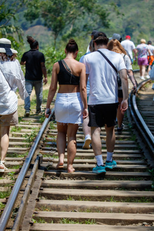 A group of people are walking down a train track. The woman is wearing a black tank top and white skirtの写真素材