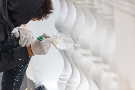 A man is painting a white railing. He is wearing a black hoodie and gloves. The railing is white and has a few black spots. The man is using a paintbrush to apply the paintの写真素材