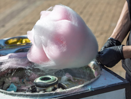 A person is blowing pink cotton candy. The cotton candy is being blown into a bowl. The bowl is on a tableの写真素材