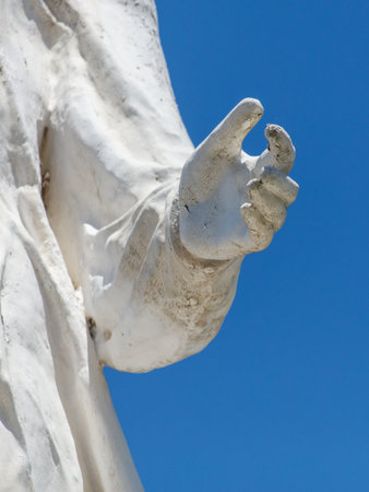 A white statue of a hand with a blue sky in the background. The statue is of Jesus Christの写真素材