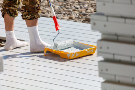 A man is painting a deck with a roller. He is wearing white socks and a camouflage shirtの写真素材