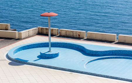 A pool with a red umbrella on top of it. The umbrella is on a pole. The pool is emptyの写真素材