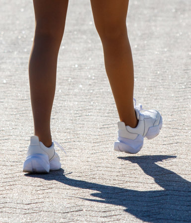 A woman is walking on a sidewalk wearing white shoes. The shoes are white and have a black soleの写真素材