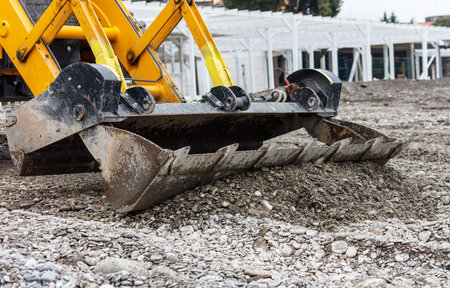 A yellow and black construction machine is digging into the ground. The machine is a backhoe loaderの写真素材