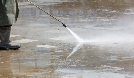 A hose is spraying water on a sidewalk. The hose is silver. The water is spraying in a spray pattern.の写真素材