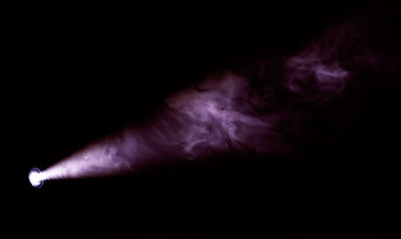 A bright light is shining on a dark background, creating a dramatic effect. The light is focused on a small object, which is surrounded by a cloud of smoke. The smoke is purple and billowingの写真素材