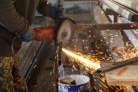 A man is using a power tool to cut metal. The sparks from the cutting process are flying everywhereの写真素材