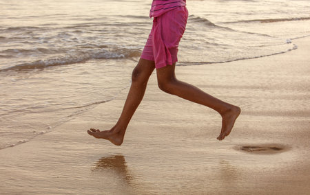 A person is running on the beach with their feet in the water. The water is calm and the sky is orangeの写真素材