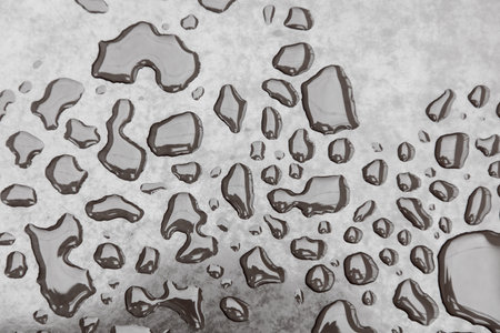 A wet surface with many small drops of water scattered across it. The drops are of various sizes and are spread out in different directions, creating a sense of movement and fluidityの写真素材