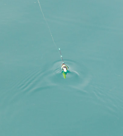 A fishing line is attached to a green and white lure. The water is calm and blue. The scene is peaceful and sereneの写真素材