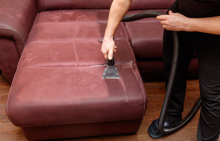 A person is cleaning a couch with a vacuum. The couch is red and has a black and white patternの写真素材