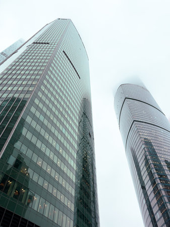 Two tall buildings with a cloudy sky in the background. The buildings are very tall and have many windowsの写真素材