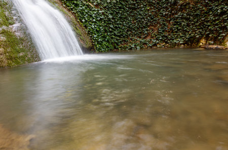 A stream of water flows down a rocky hillside. The water is murky and brown, and the rocks are scattered throughout the stream. The scene is peaceful and serene, with the sound of the waterの写真素材