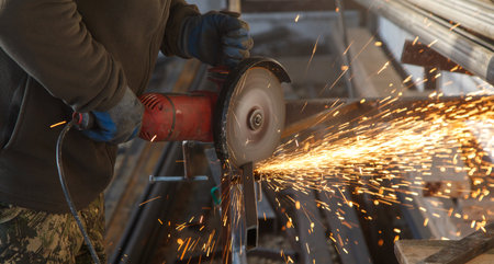 A man is using a power tool to cut metal. The sparks from the tool are flying everywhere, creating a dangerous and intense scene. The man is wearing gloves to protect his hands from the heatの写真素材
