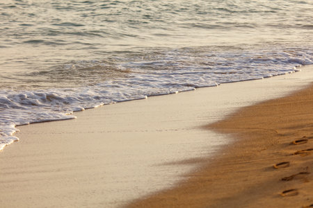 The ocean waves are crashing onto the shore, leaving a trail of footprints in the sand. The scene is serene and peaceful, with the sound of the waves providing a calming atmosphereの写真素材