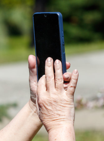 A woman is holding a cell phone and taking a picture. The phone is blue and the woman's hands are holding itの写真素材