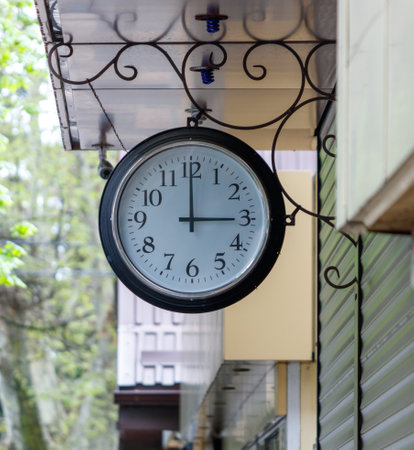 A clock hanging on a building with the hands at 3:00. The clock is black and whiteの写真素材