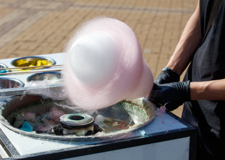 A person is making cotton candy. The cotton candy is pink and is being made in a machineの写真素材