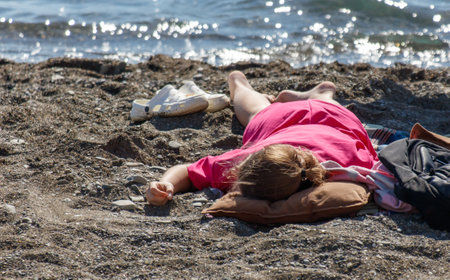 A woman is laying on the beach in a pink dress. She is wearing white shoes and a pink shirtの写真素材