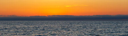 The ocean is calm and the sky is orange. The sun is setting and the water is reflecting the colors of the skyの写真素材